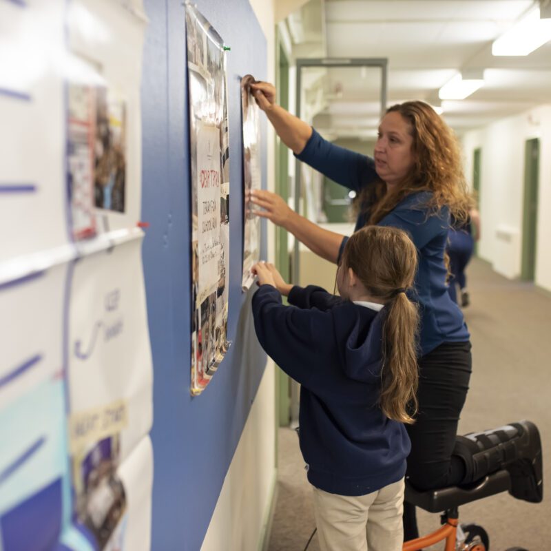 Kenneth Gordon Maplewood School Policies and Procedures - student and teacher putting a poster on the bulletin board